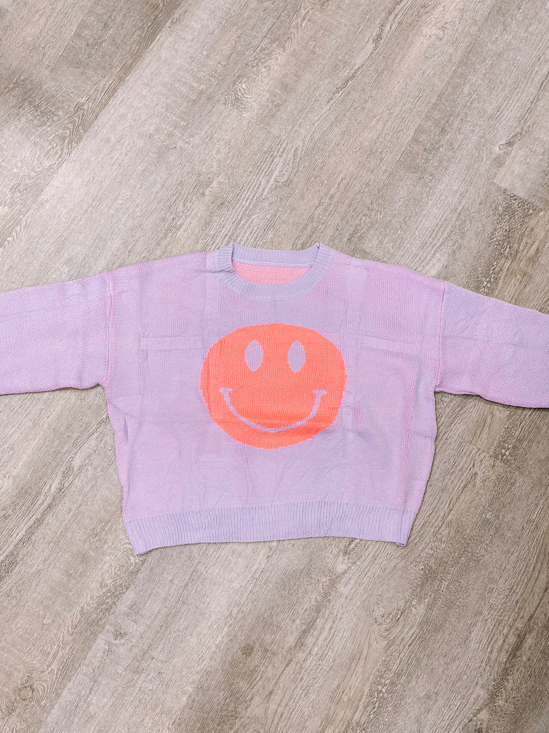 Lavender knit sweater with a large orange smiley face.
