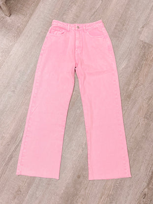 Pink wide-leg jeans laid flat on woodgrain surface.
