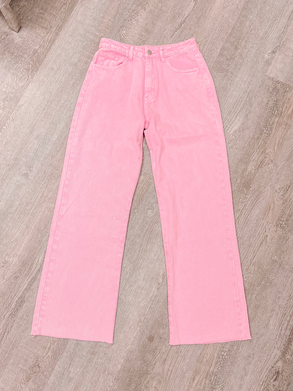 Pink wide-leg jeans laid flat on woodgrain surface.
