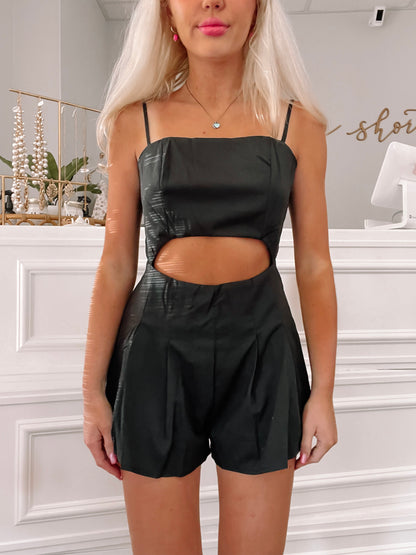Black cutout romper with pleated shorts, shown on a model against a white background.

