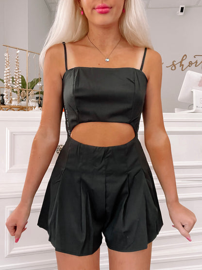 Black cutout romper with pleated shorts, shown on model.
