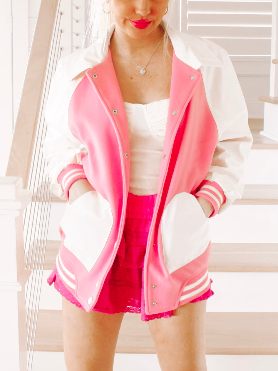 Pink and white varsity jacket with heart-shaped pockets, modeled indoors.

