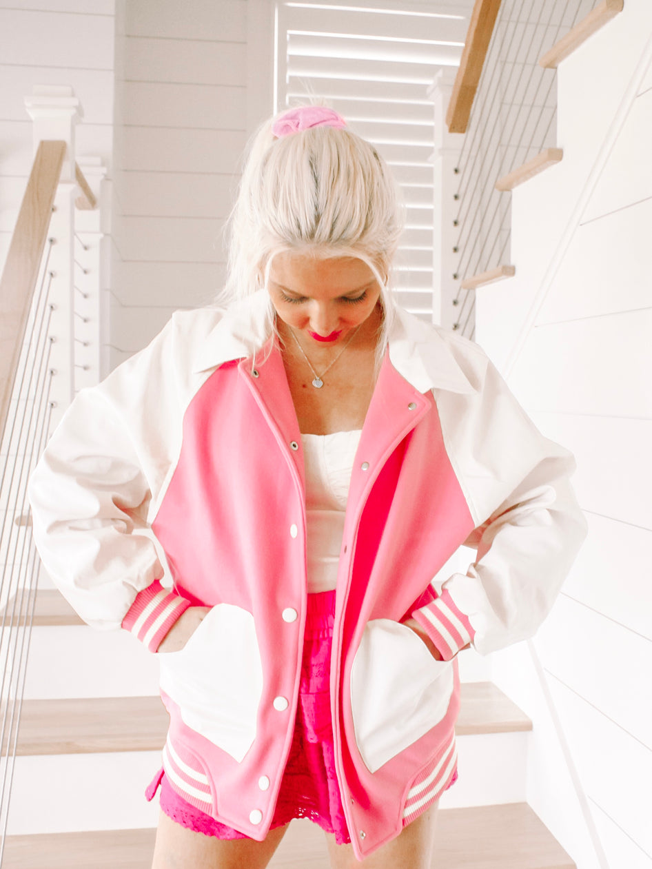 Pink and white varsity-style jacket on a model, showcased on a staircase.
