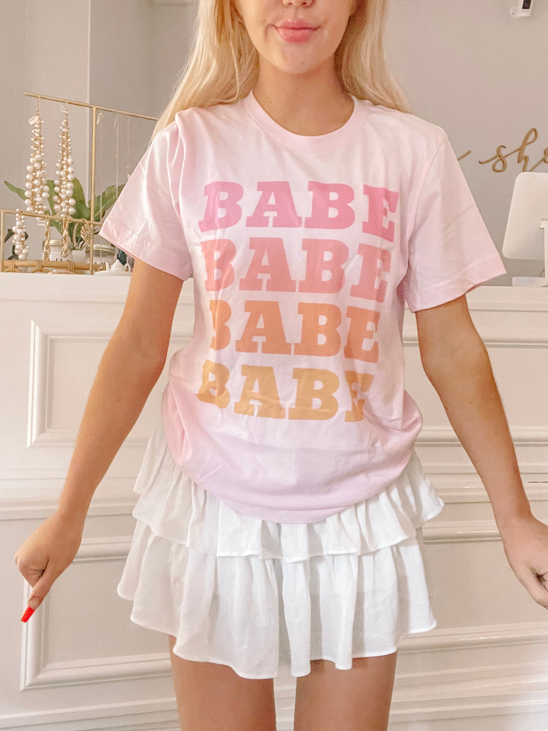 Pink pastel tee featuring a stacked "babe" graphic, styled with a white tiered mini skirt.
