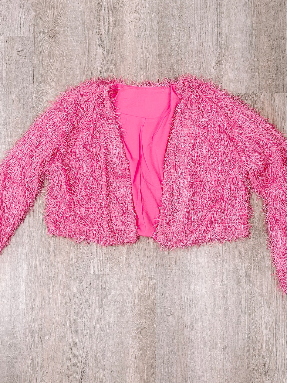 Pink fluffy cardigan laid flat on wood background.
