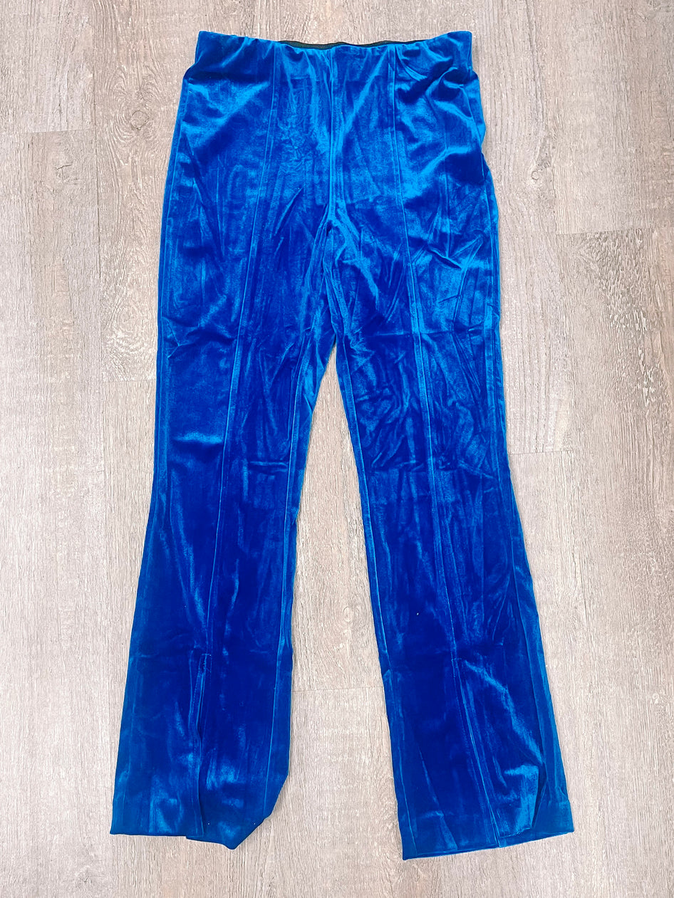 Vibrant blue velvet pants laid flat on wood; luxurious fabric texture.
