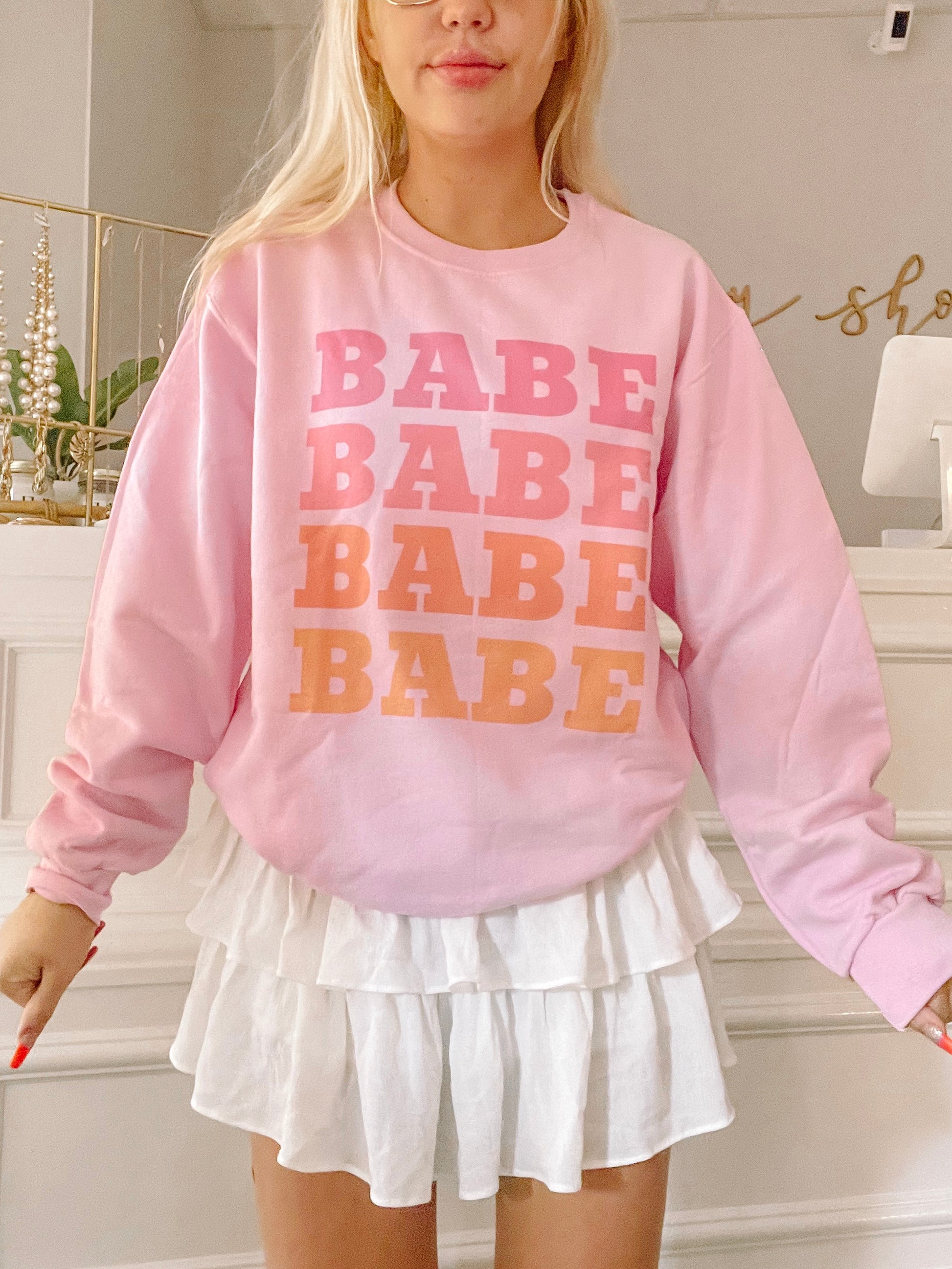 Pink sweatshirt with ombre "Babe" graphic; styled with white tiered skirt.
