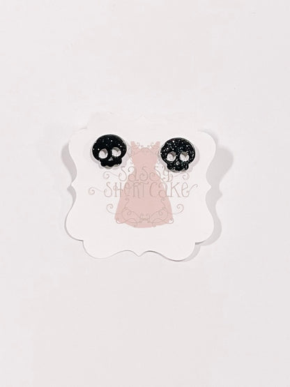 Black glitter skull stud earrings displayed on a pink tag.
