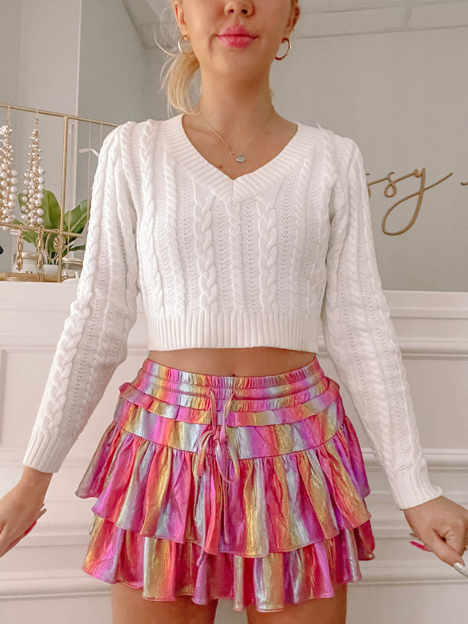 White cable knit cropped sweater paired with a vibrant metallic mini skirt.
