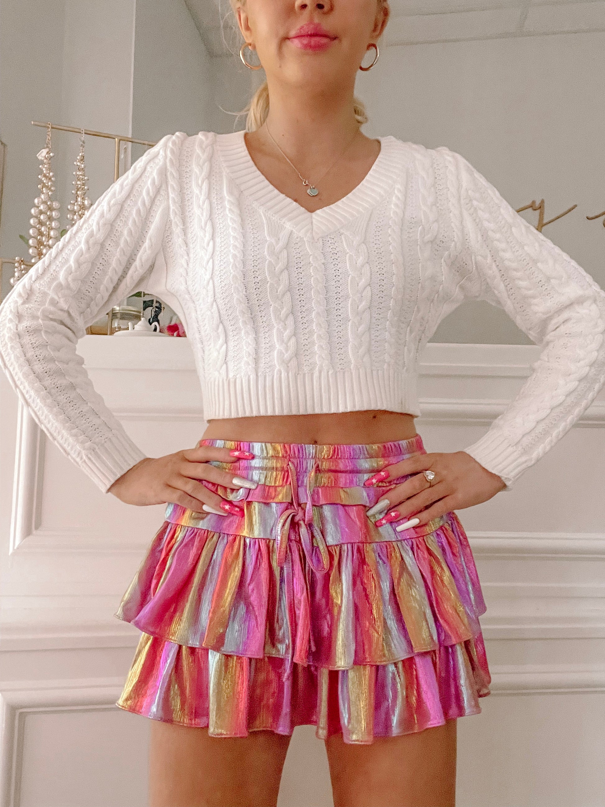 Rainbow-striped mini skirt with tiered ruffles, styled with a white cable knit sweater.

