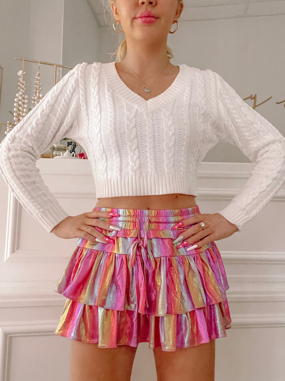Rainbow-striped mini skirt with tiered ruffles, styled with a white cable knit sweater.
