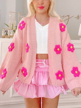 Pink knitted cardigan adorned with bright pink flowers, modeled with a pink skirt.
