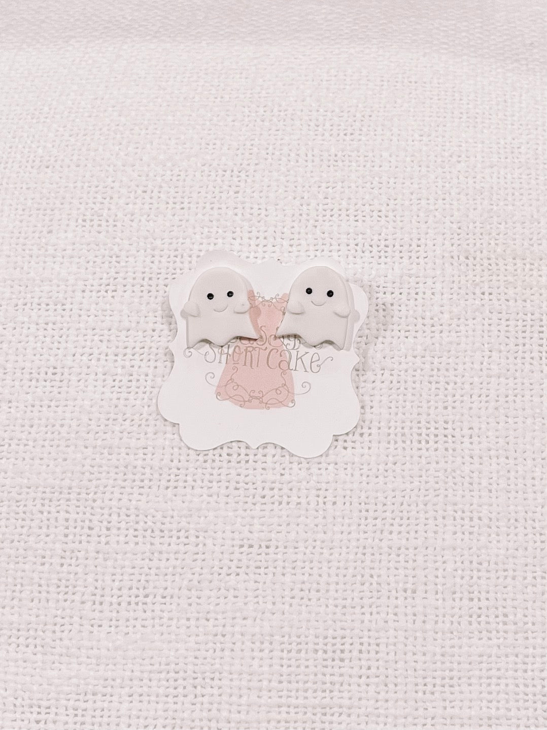 Adorable ghost-shaped Halloween earrings displayed on a white textured background.
