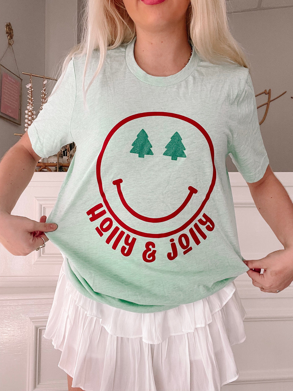 Mint green Holly Jolly Smiley Tee with red smiley face and green Christmas trees.
