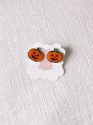 Jack-o'-lantern stud earrings displayed on a card against a textured white background.

