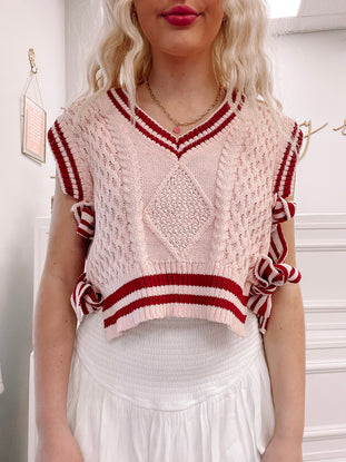 Pink cable knit cropped sweater vest with burgundy stripes, side ties, and a V-neck.
