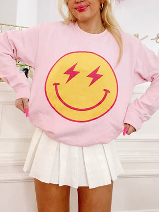 Pink crewneck sweatshirt featuring a yellow smiley face with pink lightning bolts.
