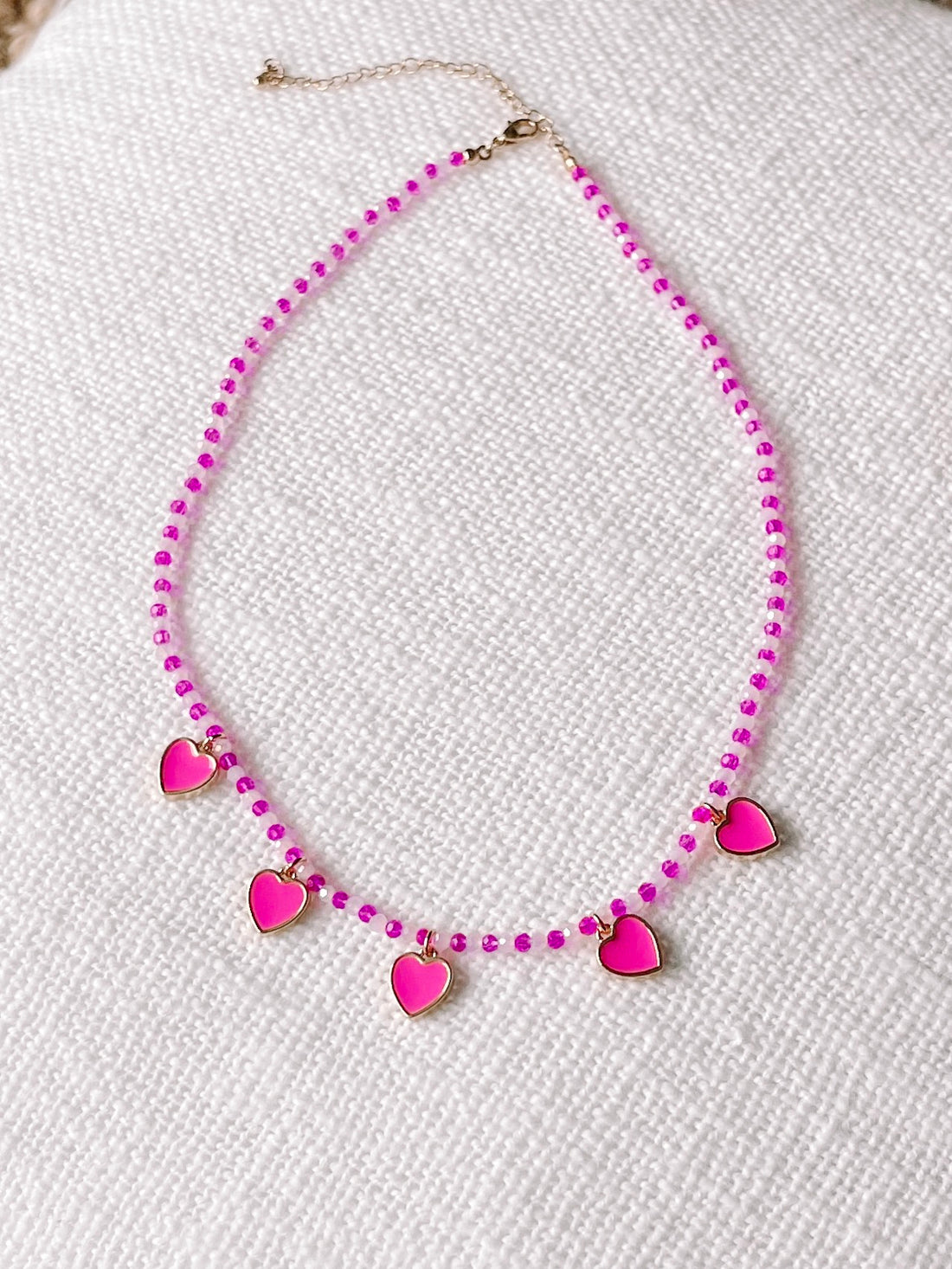 Pink and white beaded necklace with pink heart charms.
