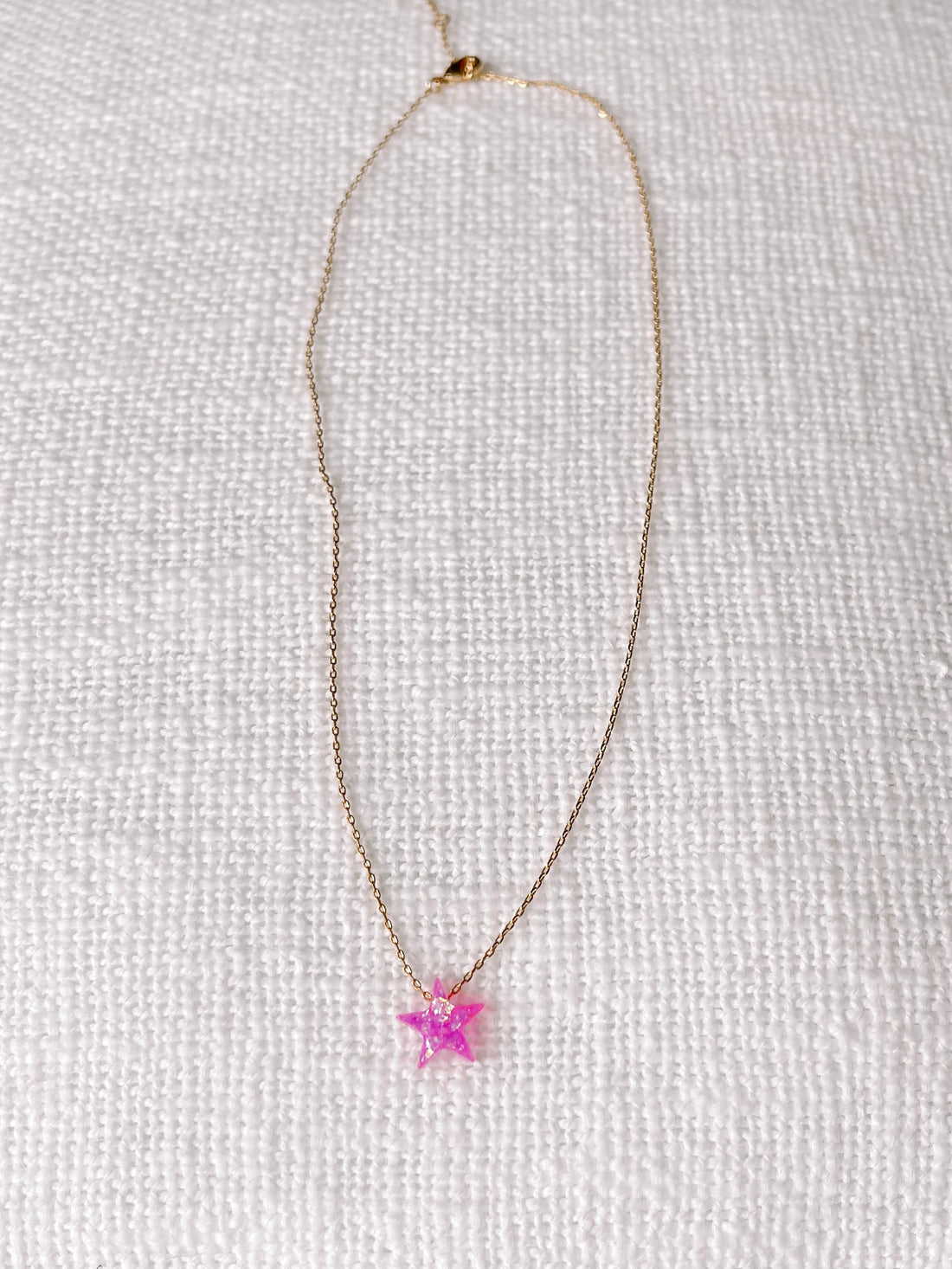 Pink opal star pendant on delicate gold chain, displayed on white textured fabric.
