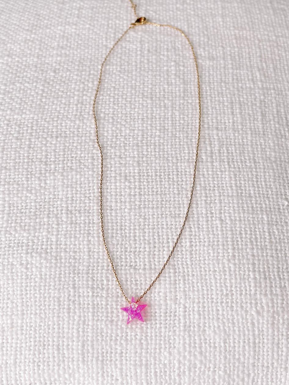 Pink opal star pendant on delicate gold chain, displayed on white textured fabric.
