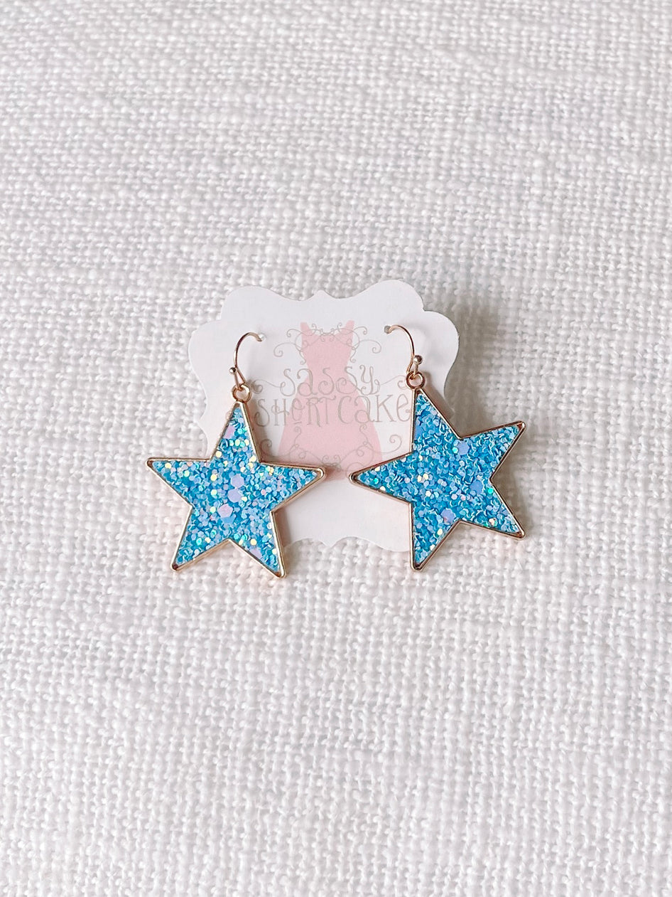 Blue Chasing Stars glitter star earrings with gold hoops.
