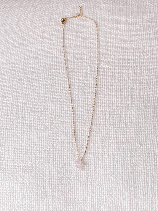 Gold chain necklace featuring a sparkly, pastel pink star charm, displayed on a white textured background.