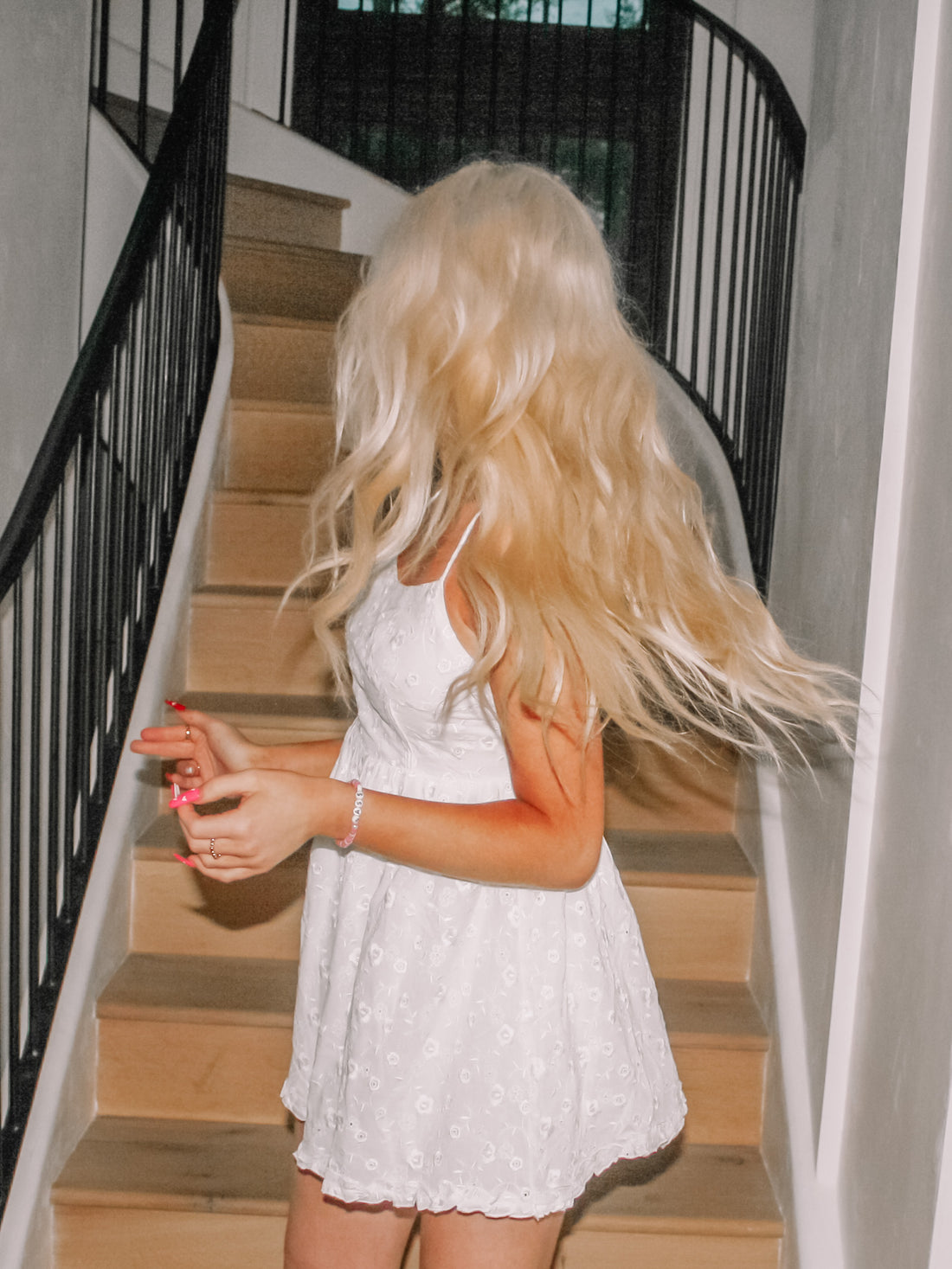 White eyelet mini dress on a model,  flowing blonde hair, wooden staircase backdrop.
