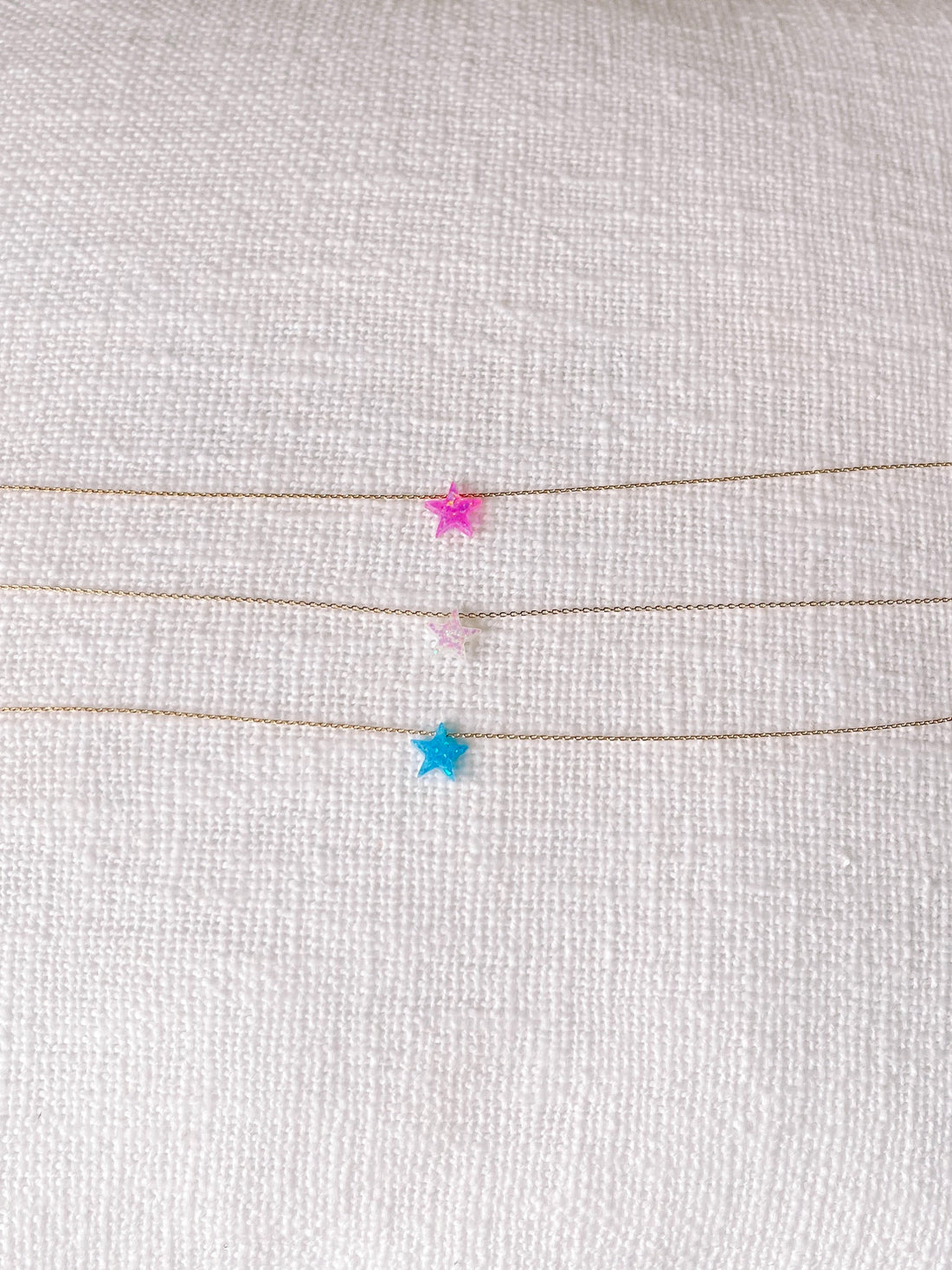 Dainty gold necklaces with colorful star accents displayed on white fabric.
