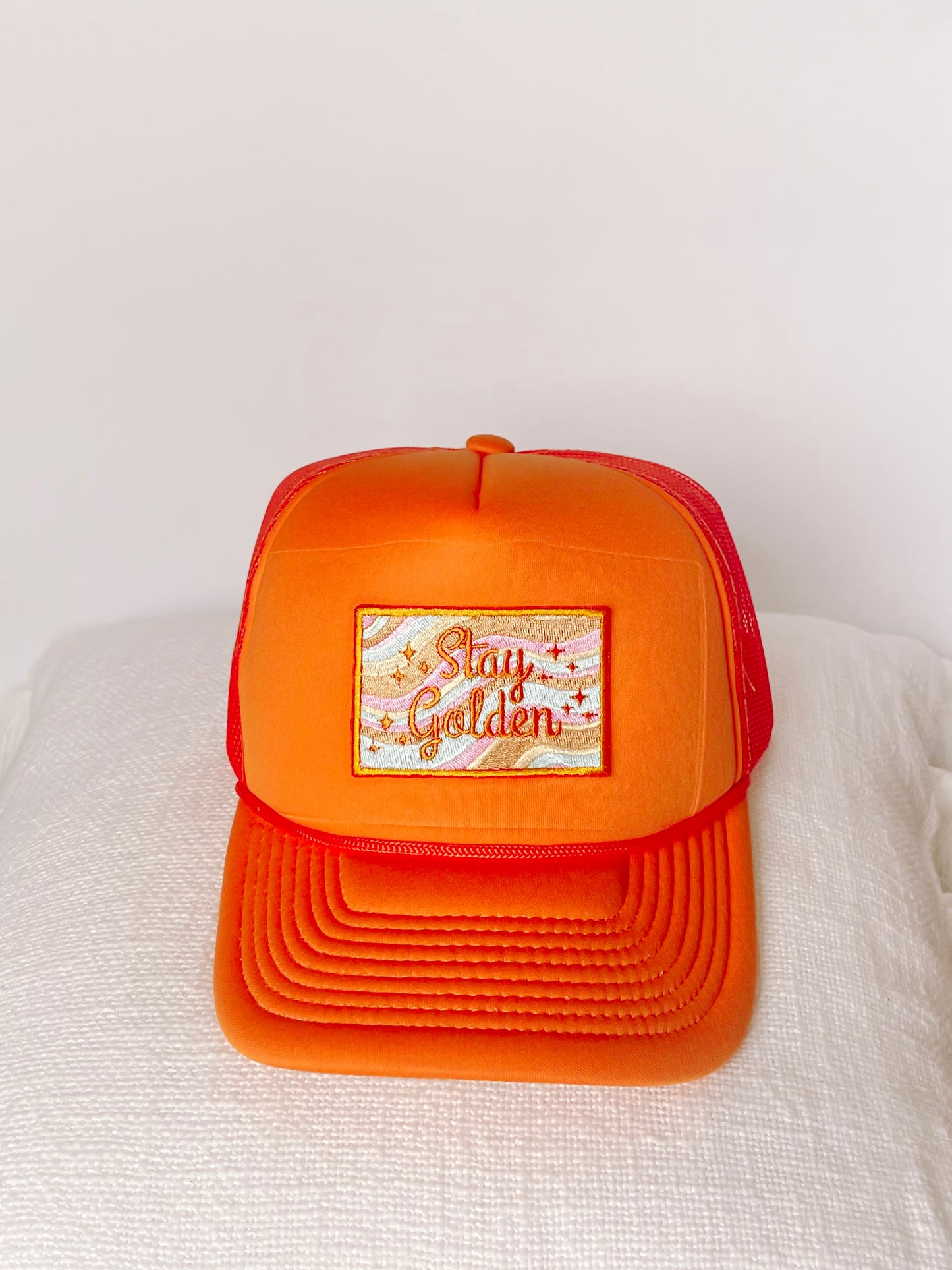 Orange Stay Golden trucker hat with embroidered patch.
