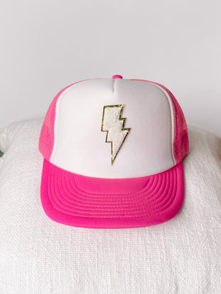 White trucker hat with hot pink bill, featuring a gold lightning bolt design.

