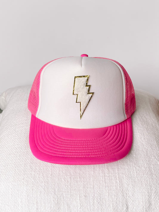 White trucker hat with hot pink bill, featuring a gold lightning bolt design.
