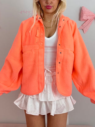 Bright orange fleece jacket styled with a white ruffled mini skirt.

