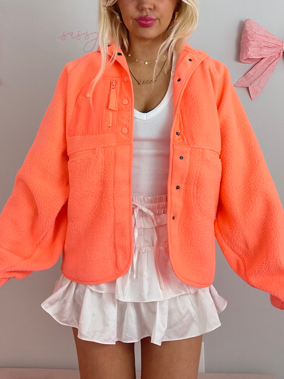 Bright orange fleece jacket styled with a white ruffled mini skirt.

