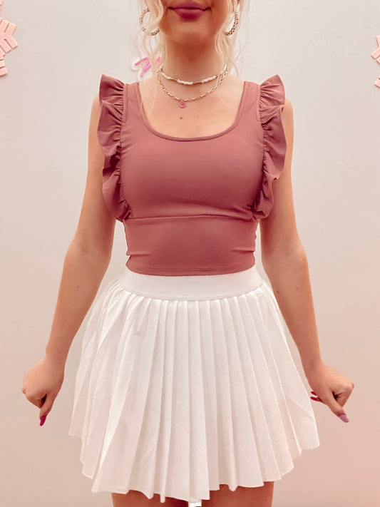 Dusty rose ruffle-trimmed crop top paired with a white pleated mini skirt.
