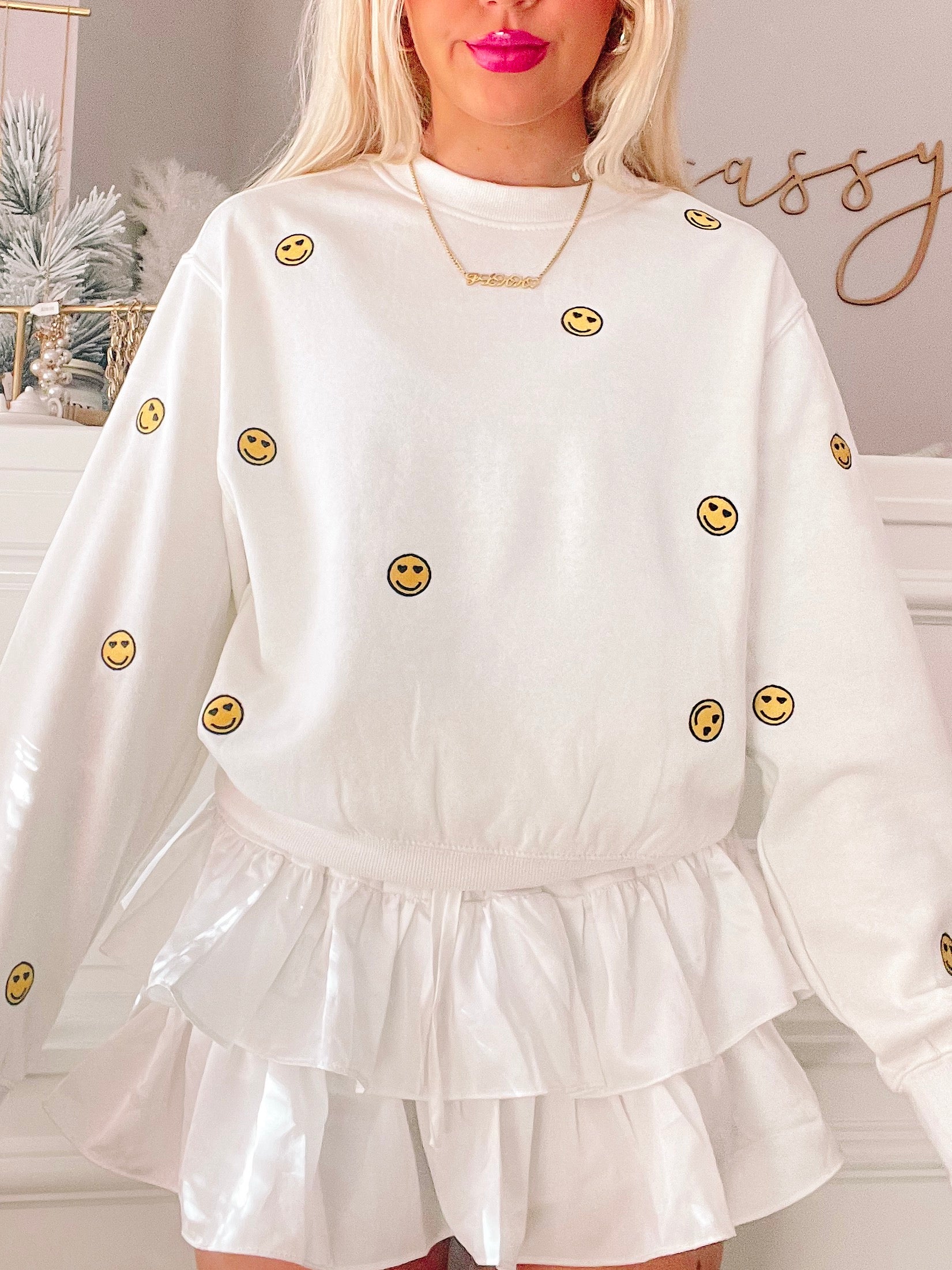 Cream crewneck sweatshirt with embroidered smiley faces, paired with a white ruffled skirt.
