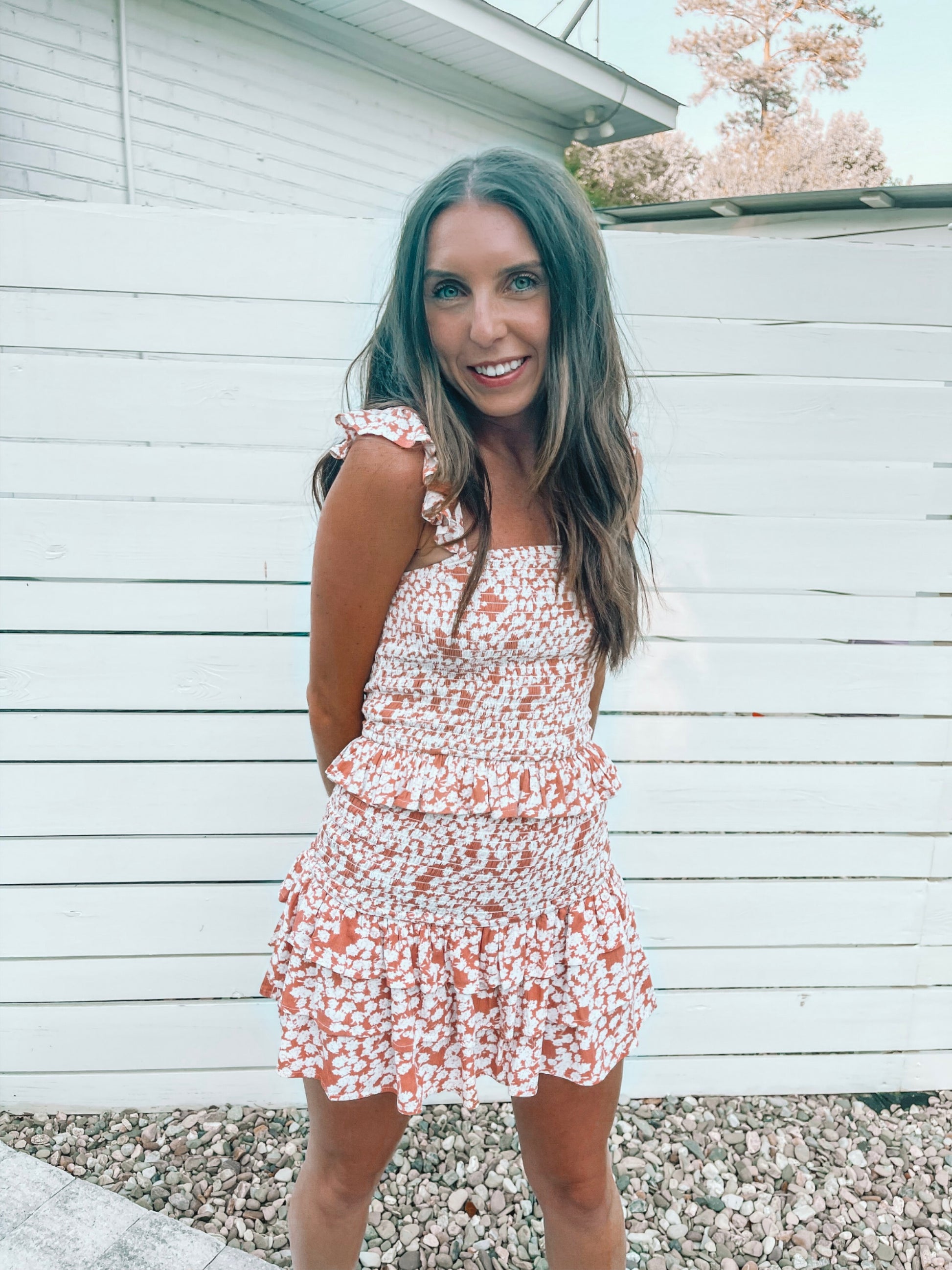 Woman modeling a terracotta floral print two-piece set against a white fence.
