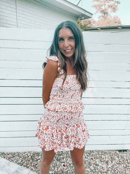 Woman modeling a terracotta floral print two-piece set against a white fence.
