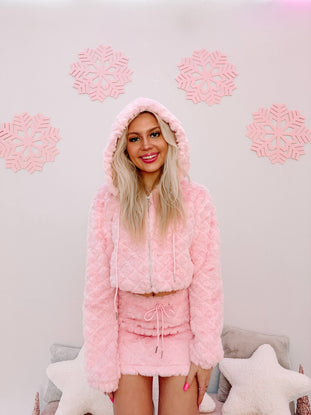 Pink fuzzy hooded zip-up jacket and mini skirt set, modeled against a pastel background.

