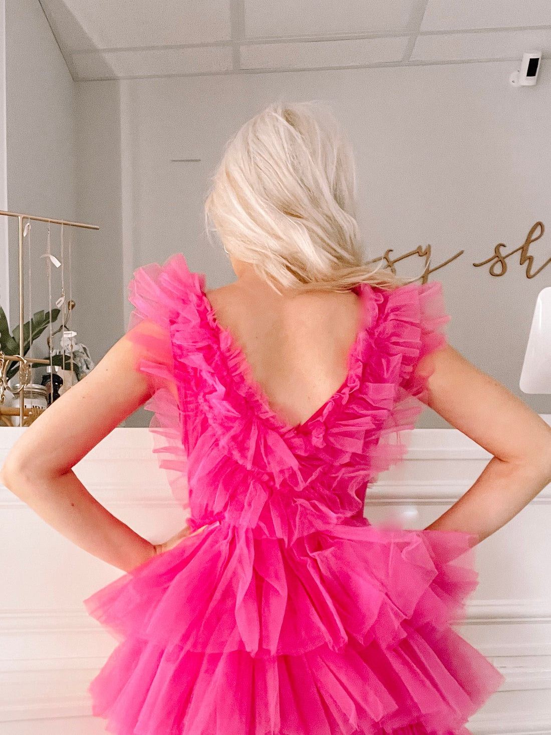 Hot pink tulle dress with layered ruffles, shown from the back in a bright interior.
