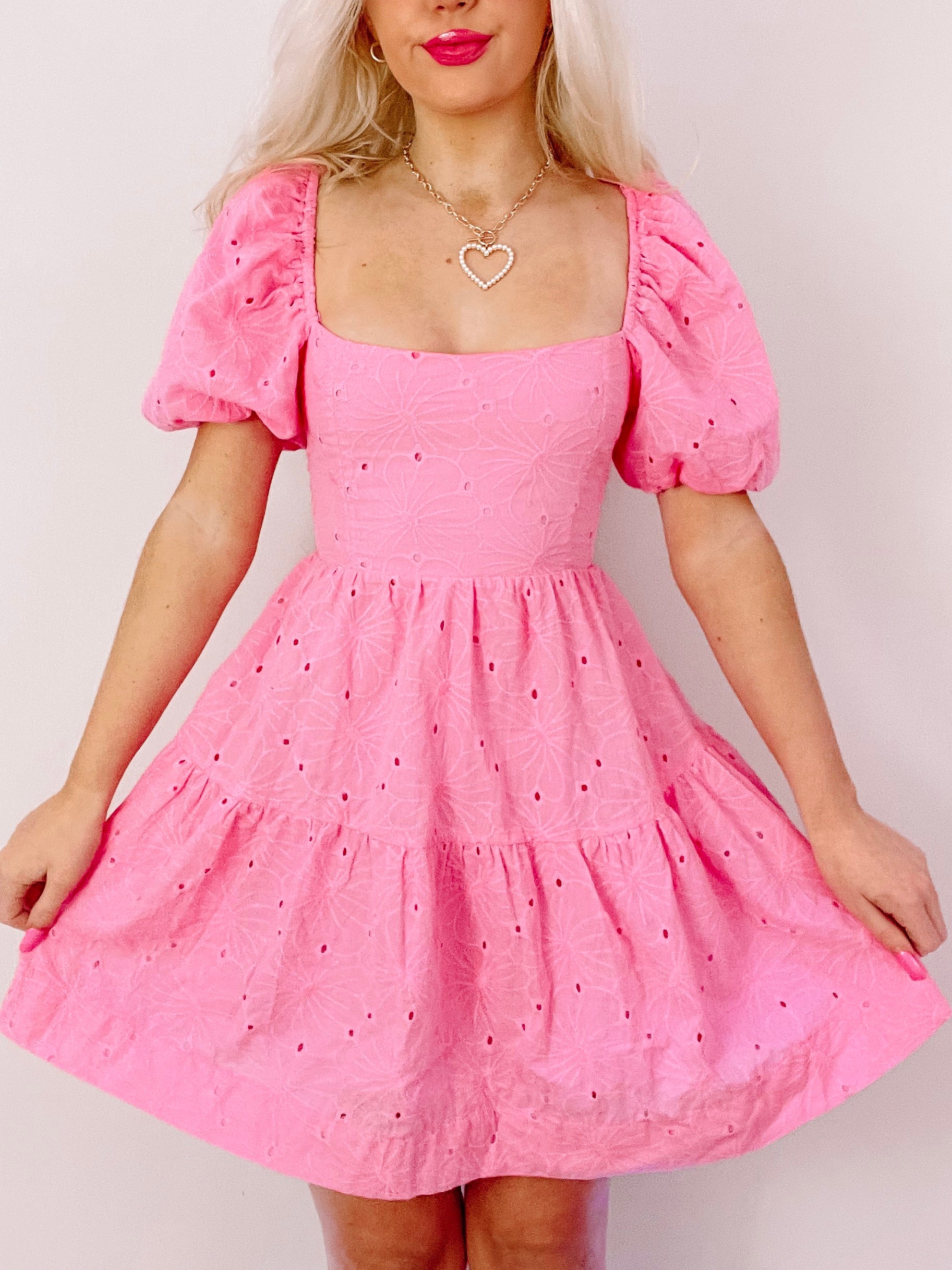 Pink eyelet mini dress with puff sleeves and tiered skirt, shown on model.
