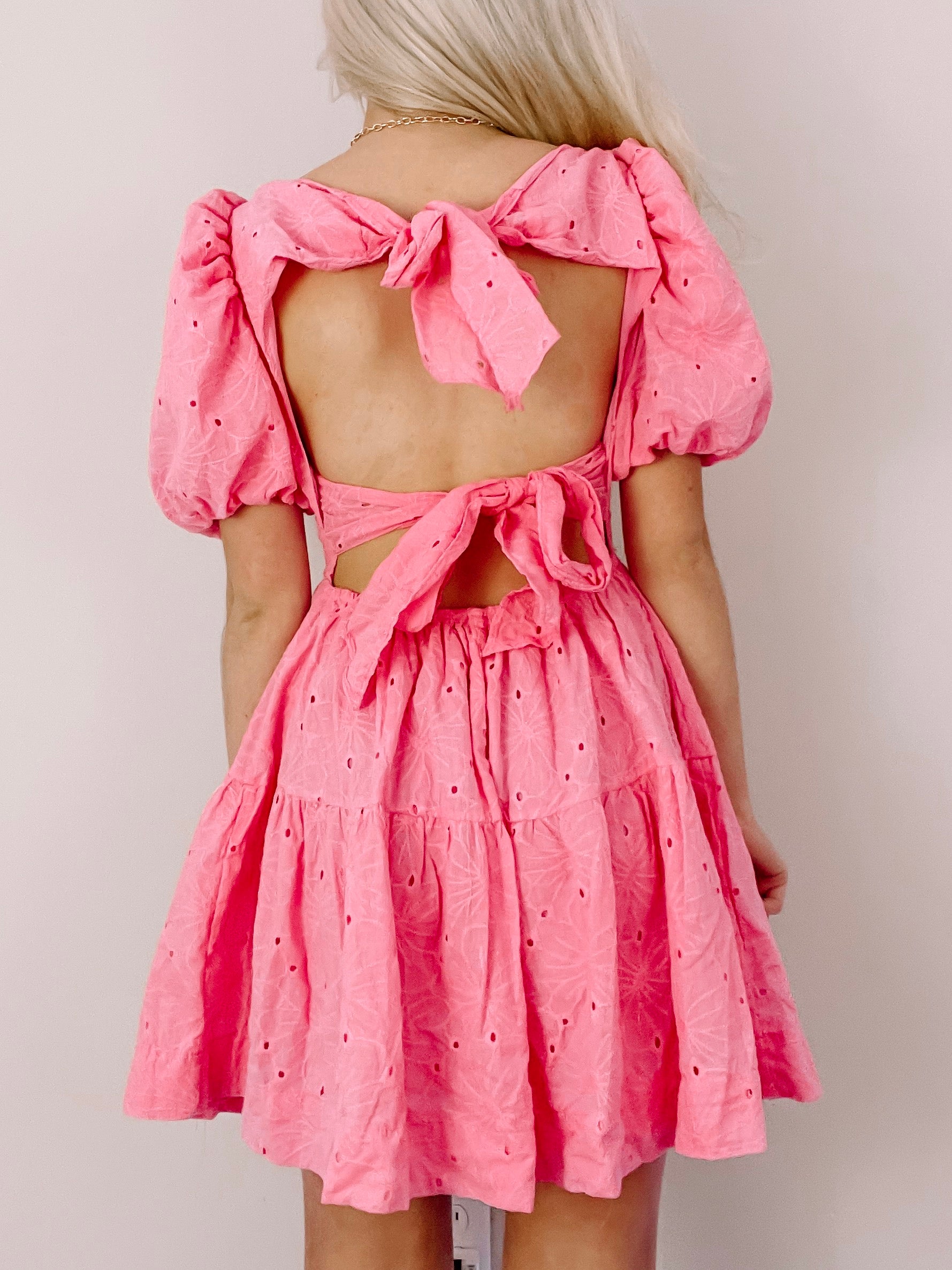 Pink eyelet mini dress with puff sleeves and a back bow detail.
