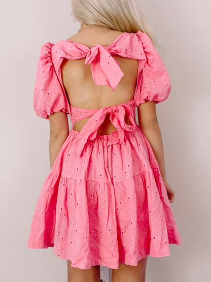 Pink eyelet mini dress with puff sleeves and a back bow detail.
