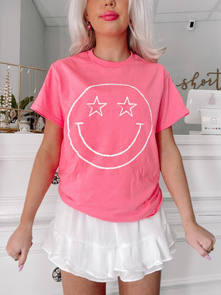 Pink Star Eyed Smiley Tee; playful graphic tee featuring a white smiley face with star eyes.
