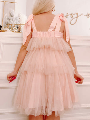 Pink tulle dress with layered skirt and satin ribbon shoulder ties, shown from the back.
