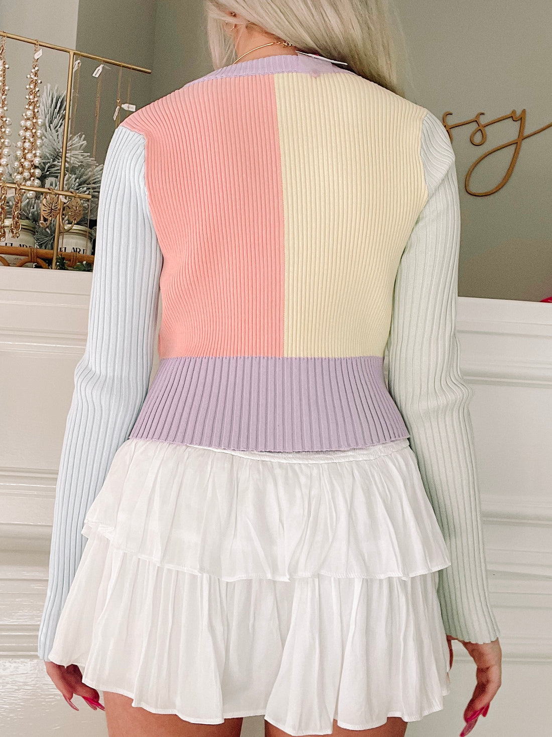 Pastel ribbed knit cardigan in peach, cream, and lavender, shown from the back with a white tiered skirt.
