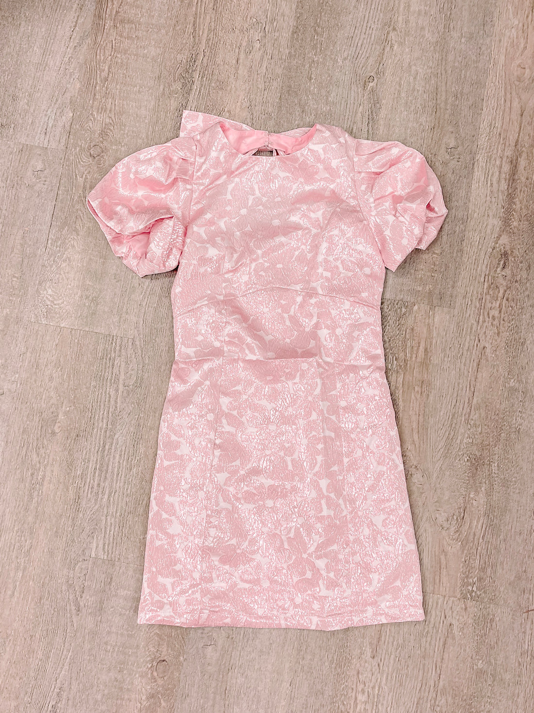 Pink mini dress with short puff sleeves and a floral pattern, laid flat on a wood background.
