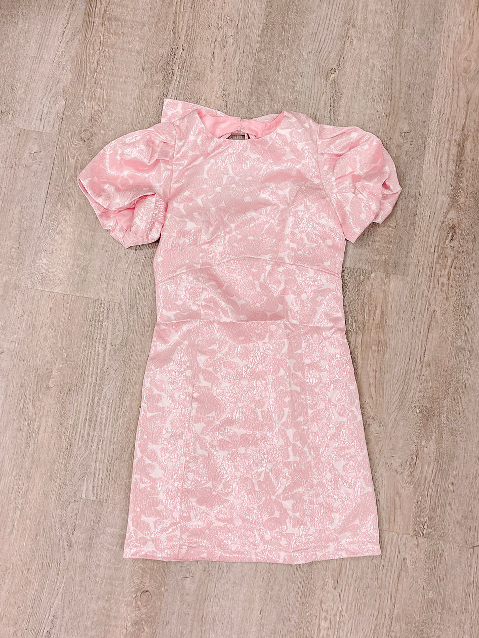 Pink mini dress with short puff sleeves and a floral pattern, laid flat on a wood background.
