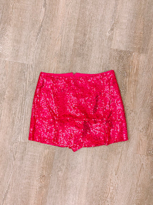Hot pink sequined mini skirt laid flat on wood.
