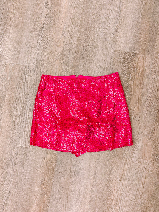 Hot pink sequined mini skirt laid flat on wood.