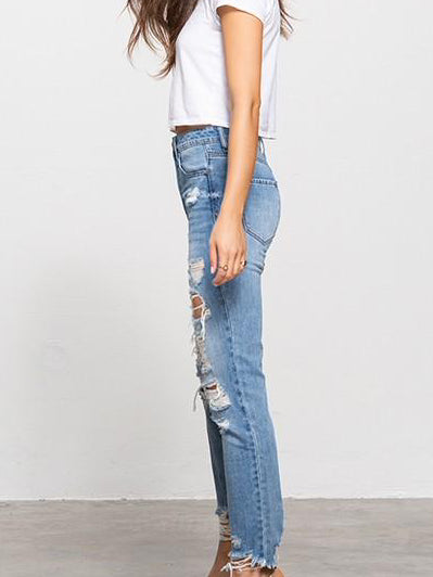 Light wash distressed jeans, featuring multiple rips and a frayed hem, shown on a model.

